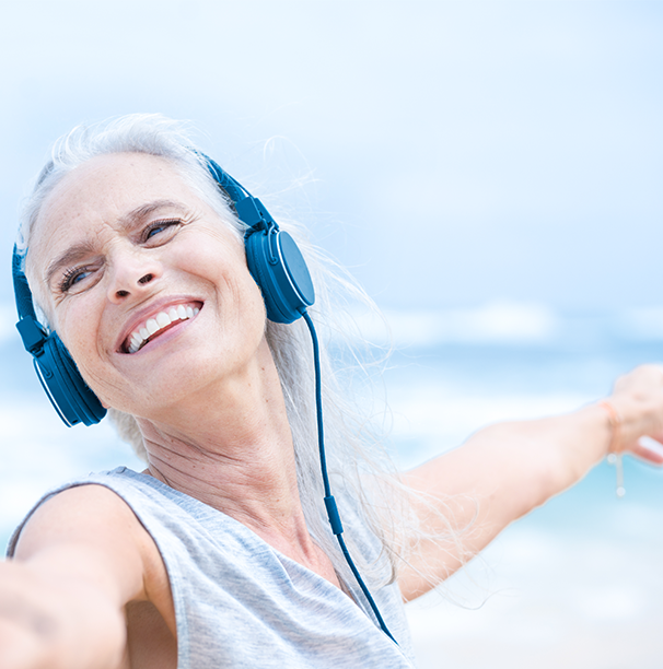 Skin Health Woman in tank top with ear phones stretching her arm out. She is by the sea.